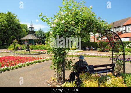 A man sits on a bench beneath a rose arch on a hot summer's day in Hall Leys Park, Matlock, Derbyshire Dales, England UK Stock Photo