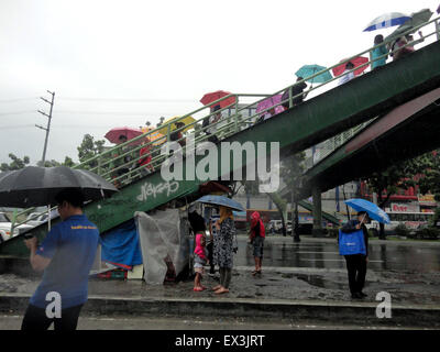 Quezon City, Philippines. 06th July, 2015. Filipinos cover themselves with umbrellas at an overpass along Quezon Avenue. Work in government offices, as well as classes in both public and private schools in Metro Manila were suspended by Malacanang late Monday afternoon due to heavy rains created by Tropical Storm Linfa (local name 'Egay'), where the storm is pummeling northern Luzon island in the Philippines. Credit:  Richard James Mendoza/Pacific Press/Alamy Live News Stock Photo