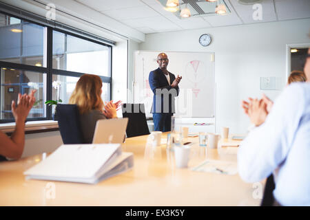 Black male executive standing at head of table in conference room smiling leading meeting Stock Photo