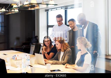 Group of young executives in conference room gathered together looking at laptop Stock Photo