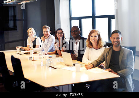 Group of executives sitting on same side of conference table posing and smiling for camera Stock Photo