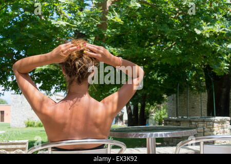 Young tanned girl sitting in a beautiful backyard wearing bikini with her hair lifted up Stock Photo