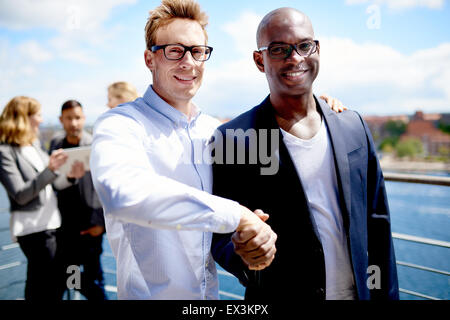 Black male colleague and white male colleague smiling at camera and shaking hands Stock Photo