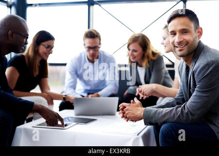 White male executive sitting and smiling at camera during a meeting with colleagues Stock Photo
