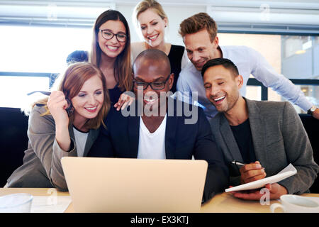 Group of executives smiling and gathered together looking at laptop Stock Photo