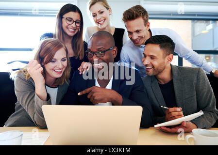 Black male executive smiling at camera with colleagues gathered around him and laptop Stock Photo