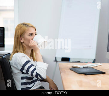 Young girl sitting at the table and drinking coffee in office Stock Photo