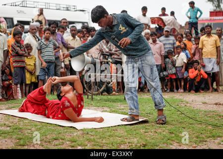 A woman performing a gymnastic stunt with a bottle in front of tens of spectators on a roadside field on the outskirts of Rajgir in Bihar, India. Stock Photo