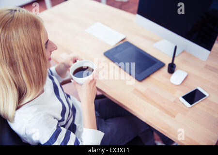 Top view portrait of a female photo editor sitting at the table and drinking coffee in office Stock Photo
