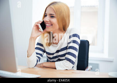 Happy young woman talking on the phone in office Stock Photo