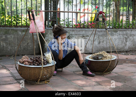 Hanoi Vietnam woman sells chestnuts while talking on her mobile phone just outside the Temple of Literature Stock Photo
