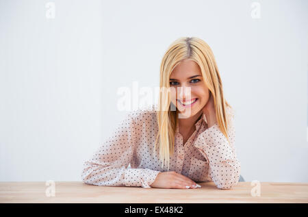 Happy young businesswoman sitting at the table over gray background and looking at camera Stock Photo