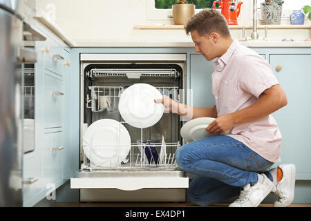 Man Loading Dishwasher In Kitchen Stock Photo