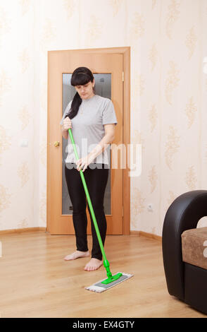 young woman in a gray T-shirt and black trousers washes wooden floor with a mop Stock Photo