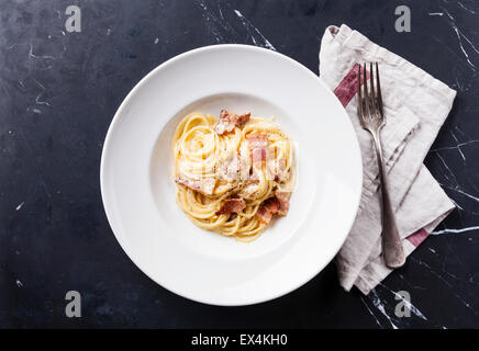 Pasta Carbonara on white plate with parmesan on dark marble background Stock Photo