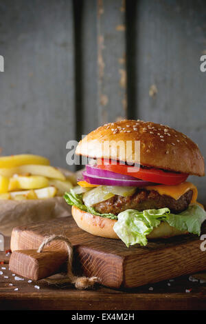 Fresh homemade burger on little cutting board with grilled potatoes, served with ketchup sauce and sea salt over wooden table wi Stock Photo