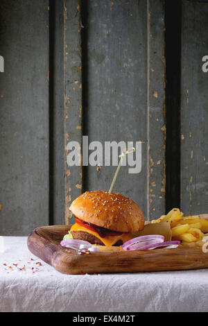 Wooden plate with fresh homemade burger and grilled potatoes over white tablecloth with gray wooden background. Dark rustic styl Stock Photo