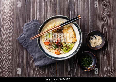 Asian noodles with tofu, oyster mushrooms and vegetables in bowl on gray wooden background