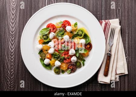 Ripe fresh colorful tomatoes salad with basil and mozarella mini on gray wooden background Stock Photo