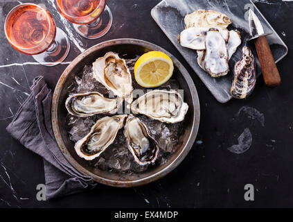Opened Oysters on metal plate and rose wine on dark marble background Stock Photo