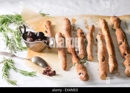 Whole and sliced black olives in vintage metal bowl with rasemary herbs and homemade grissini bread sticks on white tablecloth i Stock Photo