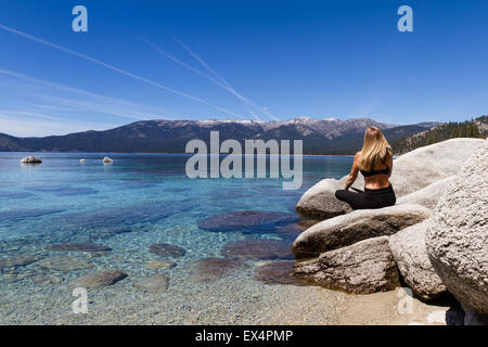 beautiful woman sitting on a boulder relaxing and enjoying a beautiful day at the lake Stock Photo