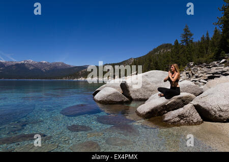 beautiful woman sitting on a boulder relaxing and enjoying a beautiful day at the lake Stock Photo
