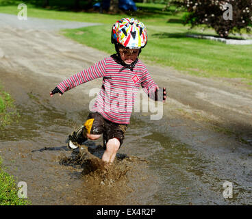A young (3 yr old) boy jumping in a muddy puddle Stock Photo
