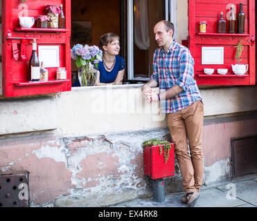 Happy young couple. A young woman looks out from the window of the house, and the man standing on the street talking with her. Stock Photo