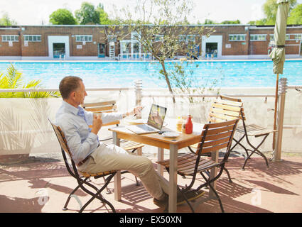 Mature Man Using Laptop at Outdoors Cafe by Swimming Pool