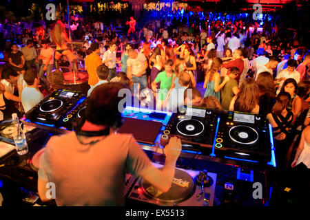 DJ on the decks / sound mixing devices and dancing nightclubbers. Athens nightclub, Greece. Stock Photo