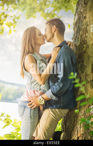 Couple in love on the lake, beneath the trees, kissing Stock Photo