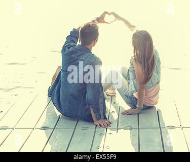Couple in love sitting on the pier, their hands show heart Stock Photo