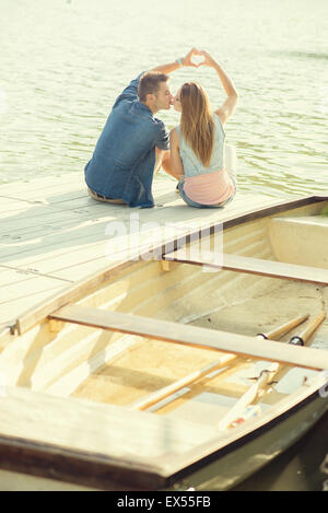 Couple in love sitting on the pier, their hands show heart Stock Photo