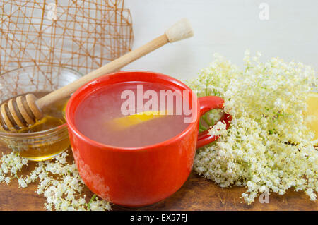 Healthy elder tea with lemon served with bowl of honey with a dipper on a table decorated with elderflowers Stock Photo