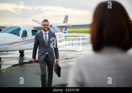 Modern businessman with briefcase walking towards his partner on background of airplane Stock Photo
