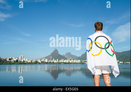 RIO DE JANEIRO, BRAZIL - MARCH 04, 2015: Man stands draped in Olympic flag in front of a skyline view of Lagoa, in Ipanema. Stock Photo