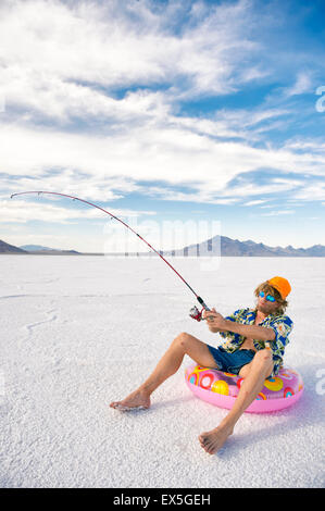 Redneck American fisherman wearing Hawaiian shirt on cheap ice fishing vacation holiday with inflatable ring in white desert Stock Photo