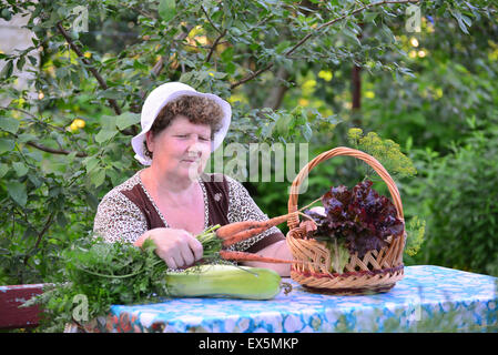 elderly woman with a basket of vegetables sitting at the table Stock Photo