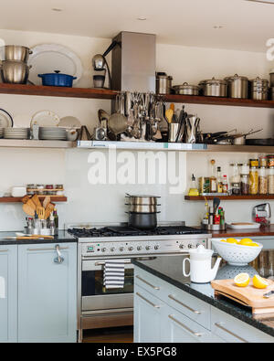 Open shleving in bright airy kitchen with range cooker and granite topped work surfaces Stock Photo