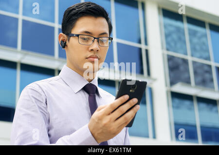 Young chinese businessman doing video conference call on smartphone and talking with bluetooth headset device in the street, loo Stock Photo