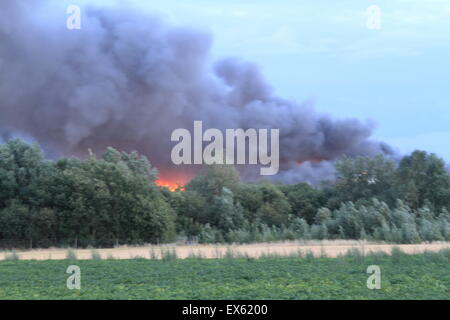 Rainham, London, UK. Tuesday 7th July 2015. Over 80 Firefighters tackle blaze in a pallet Yard in Rainham. 12 Fire engines from three Fire Services were called to the scene at around 8:00pm Tuesday evening. Kent and Essex fire and rescue services were called in to assist London Fire Brigade tackle the blaze. A stack of pallets and a number of out buildings are thought to be involved in the fire. Smoke form the blaze could be seen for miles around as winds fanned the flames. There are no reported injuries and the cause of the blaze is not yet known. Stock Photo