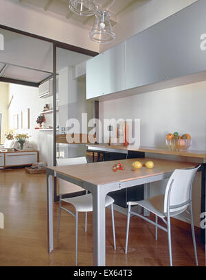 interior view of modern kitchen overlooking on the living room with wood floor,  in foreground the dining table and his chairs Stock Photo