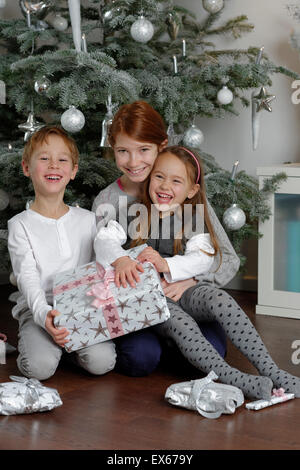 Christmas Eve, happy siblings with Christmas presents under the Christmas tree, Bavaria, Germany Stock Photo
