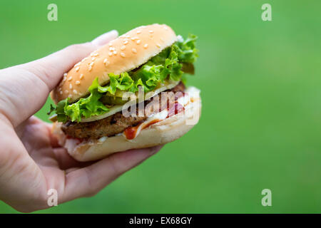 Cheeseburger in hand over green background with copy space Stock Photo