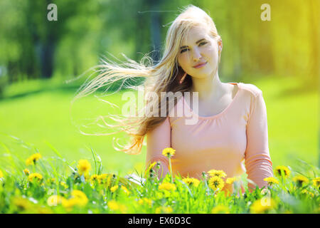 Beautiful young woman laying in spring park with dandelion flowers Stock Photo