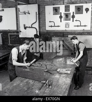 Historical, 1950s, picture shows young male engineering apprentices at a technical college working at a wooden bench doing metal work. Sections of metal piping at fixed onto the walls of the workshop as examples to follow. In post-war Britain, there was a large increase in the building of new technical colleges and other educational establishments. Stock Photo