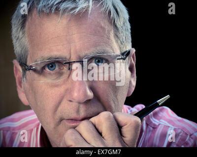 Low key powerful portrait of pensive mature businessman with hand on chin looking directly to camera Stock Photo