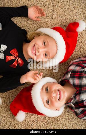 Brother (6-7) and sister (6-7) in Santa hats lying on carpet Stock Photo