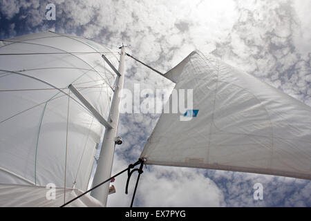 The sails of a luxury catamaran reach towards the sky and clouds Stock Photo